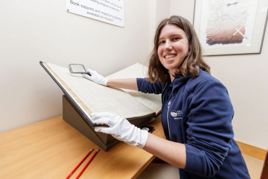 Student handling centuries old newspaper archives with gloved hands