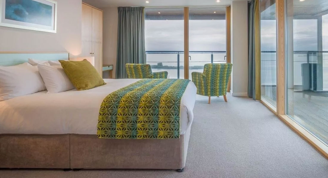 Floor to ceiling windows and a balcony in a modern bedroom at Talbot Suites in Wexford offer an expansive view of the river.