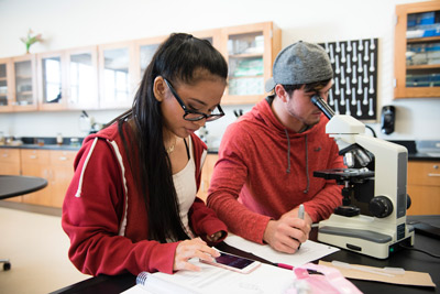 two students working on biology schoolwork with microscope