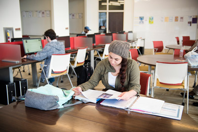 female student studying in a student common space with tables and computers