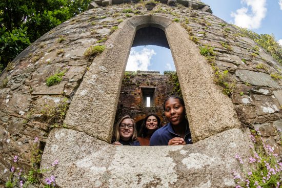 Students look out from the window of a moss-covered battlement at a castle. 