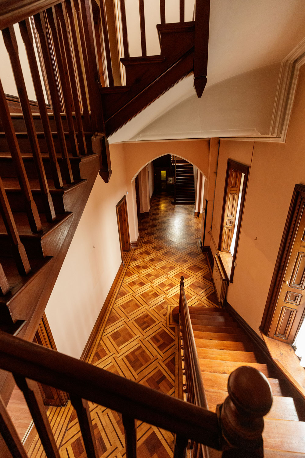 Wooden stairs lead down to a hallway with an exquisite parquet floor and large windows with broad sills and wood shutters inside.