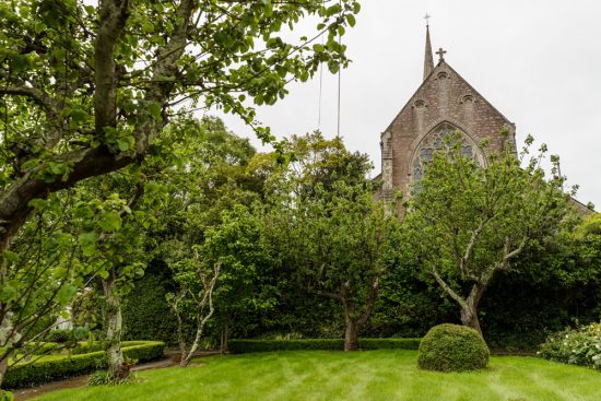 The steeple and stately facade of the church on the grounds provide scenic backdrop for the private garden. The garden has well-maintained lawns and hedges between very old trees.